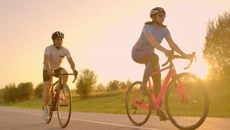 Zwei-Professionelle-Rennradfahrer-Fahren-Mit-Ihren-Fahrrädern-Einen-Hügel-Hinauf.-Handaufnahme-Von-Zwei-Starken-Radfahrerinnen-Und--männern-Beim-Training-An-Einem-Warmen,-Aber-Windigen-Sommertag